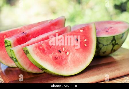 Fette di cocomero e la metà di un cocomero su un tagliere; all'aperto Foto Stock