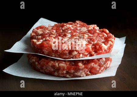 Due materie fatto a mano le carni bovine gli hamburger impilati sul bianco carta cera scura sullo sfondo di legno Foto Stock