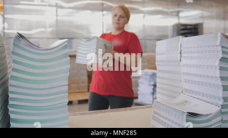 Lavoratore di sesso femminile che mette le riviste stampate in pile sul tavolo in tipografia Foto Stock