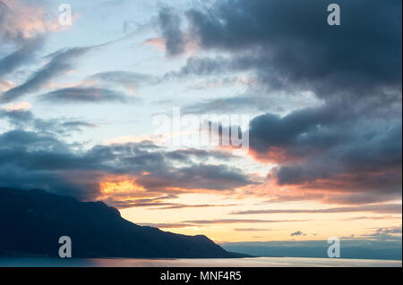 Bel tramonto sul Lago di Ginevra, Svizzera. La luce del sole riflessa sull'acqua, cielo drammatico in un panorama alpino. Foto Stock