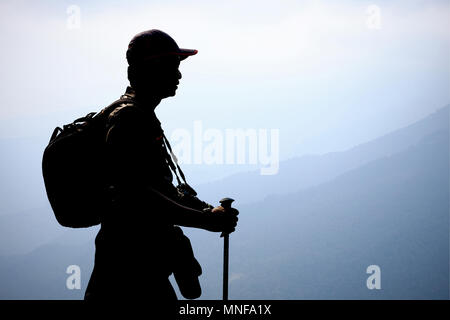 Silhouette trekker con zaino, trekking pole e fotocamera in piedi e il resto quando trekking in montagna nebbioso. Foto Stock