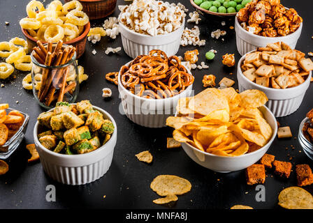 Variazione diversi spuntini malsano di cracker dolci salati di popcorn, tortillas, dadi, cannucce, bretsels, back lavagna spazio di copia Foto Stock