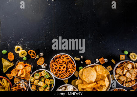 Variazione diversi spuntini malsano di cracker dolci salati di popcorn, tortillas, dadi, cannucce, bretsels, back lavagna spazio di copia Foto Stock