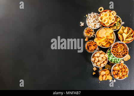 Variazione diversi spuntini malsano di cracker dolci salati di popcorn, tortillas, dadi, cannucce, bretsels, back lavagna spazio di copia Foto Stock