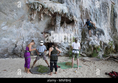 Turisti e visitatori di vivere lo sport arrampicata sulle rocce calcaree di Thailandia Railey Beach. Foto Stock