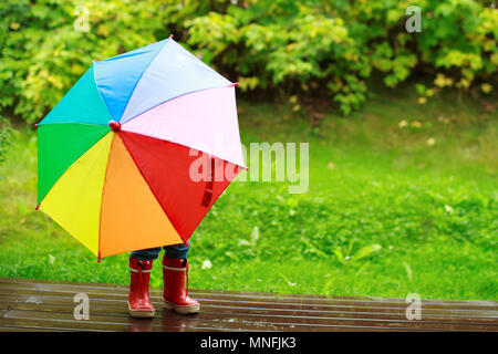 Giocoso bambina di nascondersi dietro a ombrello coloratissimo all'aperto Foto Stock
