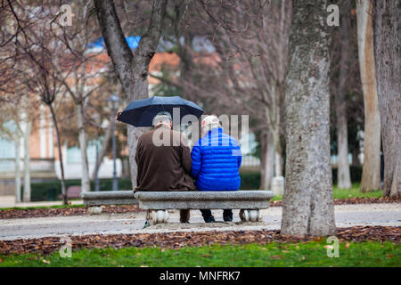 Coppia senior su un banco in un parco della città in un giorno di pioggia Foto Stock