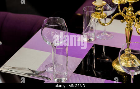 Bicchieri e un candelabro su un tavolo di vetro in un ristorante. Ambiente romantico Foto Stock