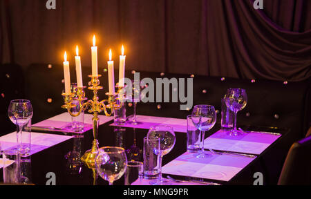 Bicchieri e un candelabro su un tavolo di vetro in un ristorante. Ambiente romantico Foto Stock