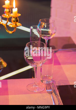 Bicchieri e un candelabro su un tavolo di vetro in un ristorante. Ambiente romantico Foto Stock