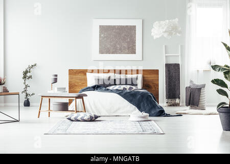 Dipinto di grigio su bianco parete sopra il letto in camera da letto spaziosa con interni scaletta, lampada di design e panca in legno Foto Stock