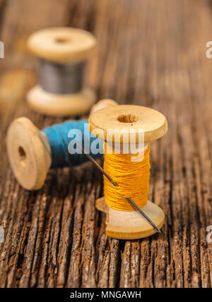 Fili colorati e ago su sfondo di legno Foto Stock