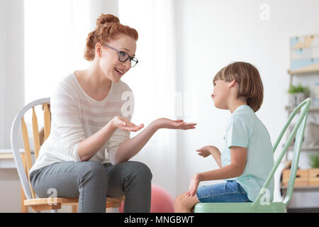 Psicoterapeuta sorridente parlando con il ragazzo autistico seduto sulla sedia di menta durante la psicoterapia Foto Stock