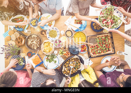 Uomo in maglietta modellata condivide le patate al forno con gli amici durante il gustoso pranzo vegetariano Foto Stock