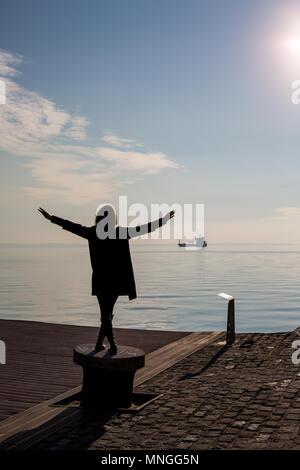 Vista posteriore di ballare il giovane bella montare donna con capelli corti sul polo di docking in Salonicco, Grecia. Vista posteriore con il blu del mare e del cielo e la nave in th Foto Stock