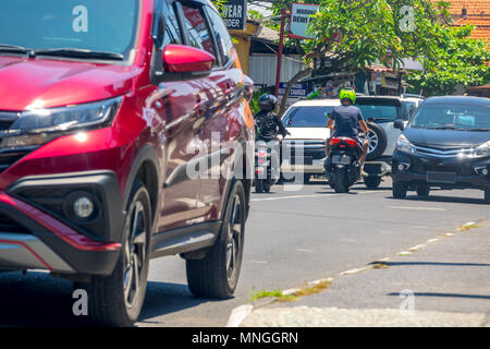 Indonesia. Strada di città sull'isola di Bali. Giornata di sole. Auto e scooter Foto Stock