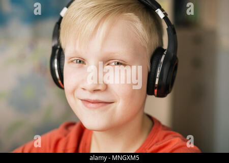 Bionda sorridente ragazzo ascoltando musica in cuffia, sorridente e guardando la fotocamera. Foto Stock