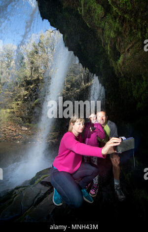 Quattro le cascate a piedi vicino Pontneddfechan in Brecon Beacons - una famiglia a piedi dietro l'Sgwd yr Eira falls (cadute di neve) sul Fiume Hepste Foto Stock