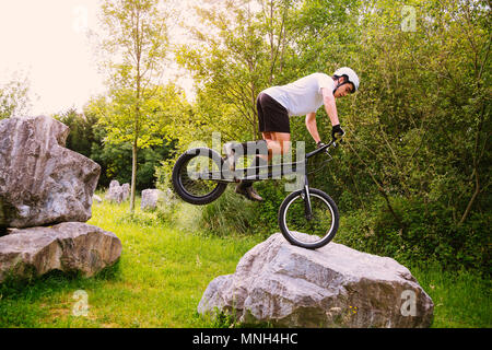 Giovane ciclista jumping con la ruota anteriore di una bicicletta di prova su una roccia Foto Stock