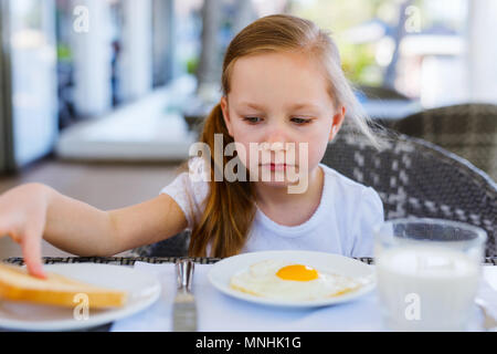 Adorabile bambina mangiare uova fritte per una prima colazione al ristorante Foto Stock