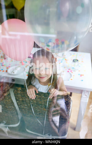 Adorabile bambina con palloncini colorati a bambini festa di compleanno di guardare attraverso una finestra Foto Stock