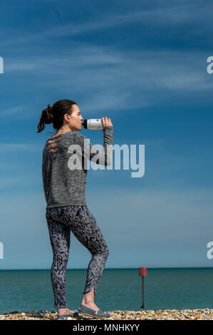 Sportivo da donna in piedi sul mare di appoggio e di bere da uno sport di acqua in bottiglia Foto Stock