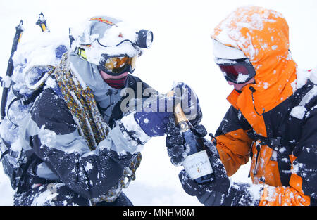 Due alpinisti ricoperta di neve di aprire una bottiglia di champagne in inverno blizzard, per celebrare con successo una salita in Chamonix, Alta Savoia, Francia Foto Stock