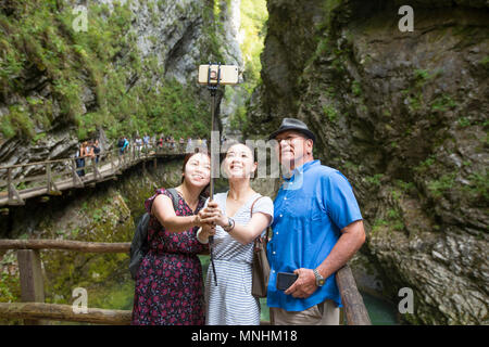 Turisti asiatici stanno prendendo un gruppo selfie con uno smart phone su un bastone selfie in gola gorge, Slovenia. La gola gorge è un burrone nelle immedia Foto Stock