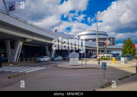 MINSK, Bielorussia - 01 Maggio 2018: veduta esterna di automobili parcheggiate e circolante all'invio di Minsk edificio aeroportuale in un giorno nuvoloso con una torre di controllo dietro Foto Stock