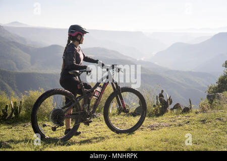 Vista laterale della donna in piedi con mountain bike in ambiente naturale con le montagne sullo sfondo, pena del Aire, Huasca de Ocampo, hidalgo, Messico Foto Stock