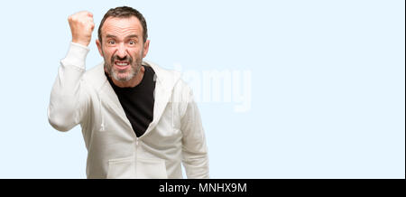 La mezza età uomo di indossare abbigliamento sportivo irritato e arrabbiato esprimendo emozione negativa, arrabbiato con qualcuno isolate su sfondo blu Foto Stock