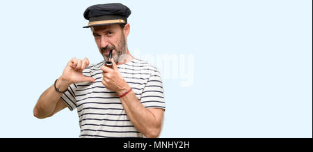 Sailor capitano uomo fumare una tubazione di tabacco orgogliosi, eccitato e arrogante, dispositivo di puntamento con la vittoria di fronte isolate su sfondo blu Foto Stock