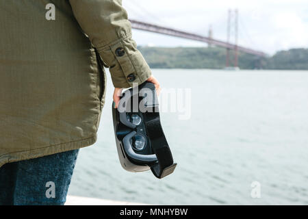 La ragazza è in possesso di occhiali per realtà virtuale. Ponte 25 Aprile a Lisbona in Portogallo in background Foto Stock