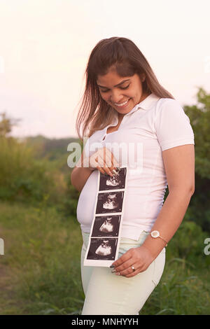 Sorridenti donna incinta con ultrasuoni stampa su sfondo natura Foto Stock