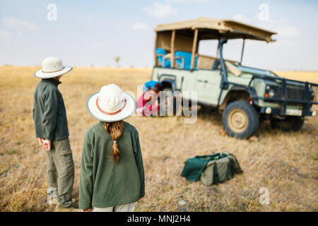 I bambini in Kenya safari al mattino game drive in veicolo aperto guardando guide masai cambiando il pneumatico sgonfio Foto Stock