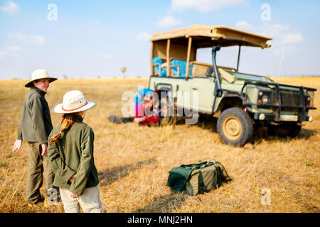 I bambini in Kenya safari al mattino game drive in veicolo aperto guardando guide masai cambiando il pneumatico sgonfio Foto Stock