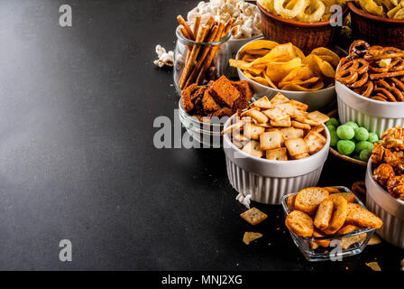 Variazione diversi spuntini malsano di cracker dolci salati di popcorn, tortillas, dadi, cannucce, bretsels, back lavagna spazio di copia Foto Stock