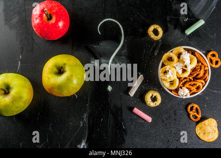 Variazione diversi spuntini malsano di cracker dolci salati di popcorn, tortillas, dadi, cannucce, bretsels, back lavagna spazio di copia Foto Stock