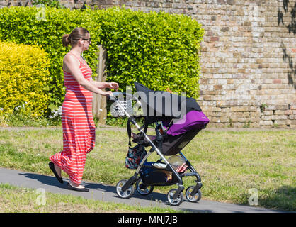 Giovane donna spingendo un bimbo nel passeggino indossando abiti estivi in un caldo giorno d'estate. Foto Stock