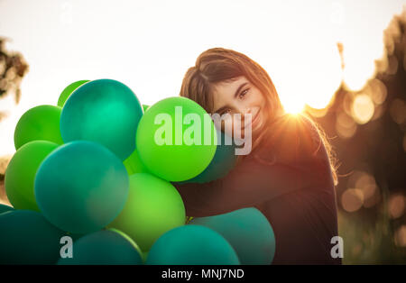 Ritratto di una bella ragazza sorridente all'aperto avvolgente grande pila di aria verde palloncini, si prepara a celebrare la festa di compleanno, felice infanzia spensierata Foto Stock