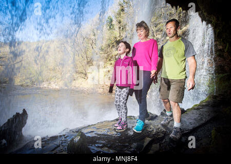 Quattro le cascate a piedi vicino Pontneddfechan in Brecon Beacons - una famiglia a piedi dietro l'Sgwd yr Eira falls (cadute di neve) sul Fiume Hepste Foto Stock