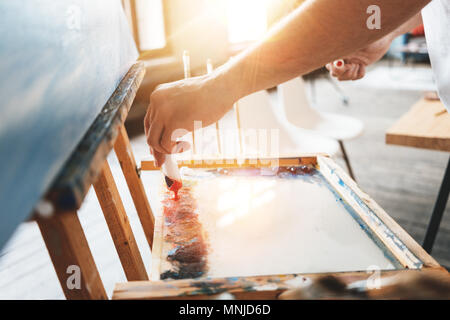 Man mano dell artista closeup spremitura di vernice da un tubo su una tavolozza. Pittore olio mix di colori di vernice sulla tavolozza in officina. Effetto Flare Foto Stock