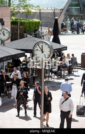 Canary Wharf, orologi visualizza il tempo appena prima delle 12pm al di fuori della stazione della metropolitana con i dipendenti fresatura intorno godendosi il sole Foto Stock