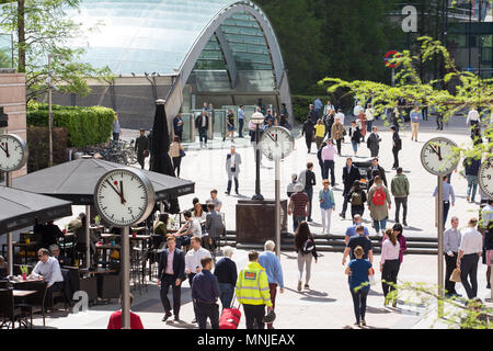 Canary Wharf, orologi visualizza il tempo appena prima delle 12pm al di fuori della stazione della metropolitana con i dipendenti fresatura intorno godendosi il sole Foto Stock