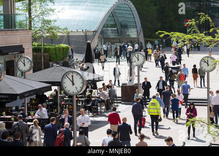 Canary Wharf, orologi visualizza il tempo appena prima delle 12pm al di fuori della stazione della metropolitana con i dipendenti fresatura intorno godendosi il sole Foto Stock