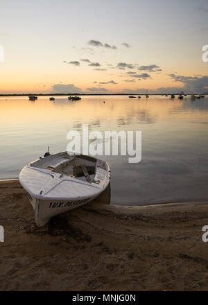 Spiaggiata skiff al tramonto con ancorate barche a vela e le nuvole riflessione a Estany des Peix lagoon a La Savina (Formentera, isole Baleari, Spagna) Foto Stock