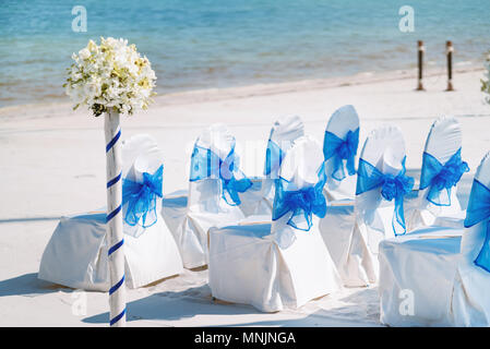 Il bianco casuale spandex sedie con coperchio blu organza di decorazione a ghigliottina in attesa di spiaggia matrimoni setup Foto Stock