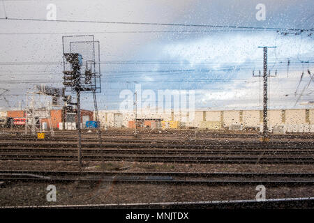 Con tempo umido. Guardando fuori attraverso una finestra del treno con gocce di pioggia sul vetro a binari ferroviari in un giorno di pioggia, Doncaster, England, Regno Unito Foto Stock