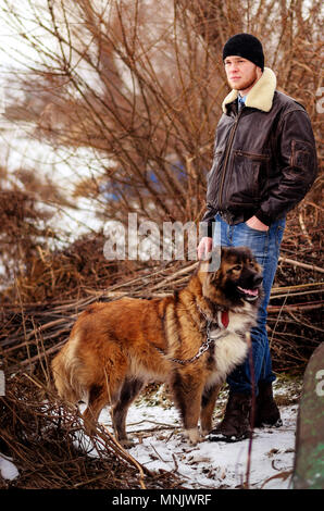 Un giovane uomo in inverno si erge insieme con un Pastore del Caucaso. Foto Stock