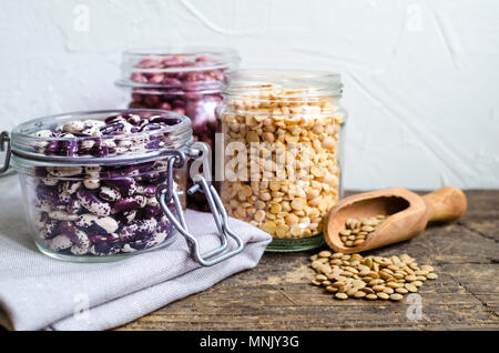 Assortimento di organico secco fagioli e lenticchie in vasetti di vetro su tavola in legno rustico. Varietà di legumi di greggio. Dieta bilanciata, cucina vegetariana e pulire Foto Stock